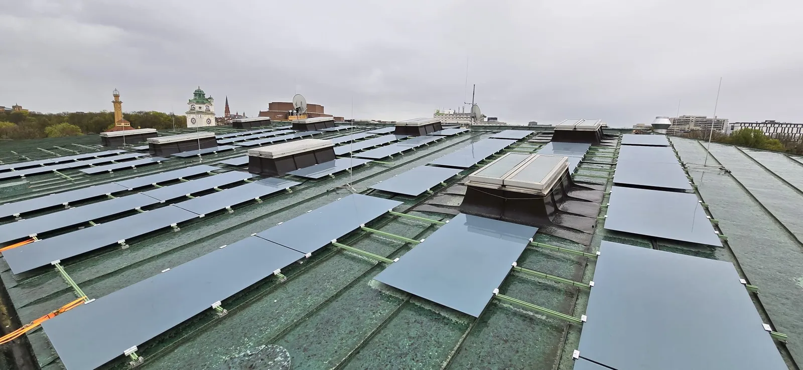 Fertig montierte, rahmenlose PV-Module auf dem grünen Kupferdach des Deutschen Museums, im Hintergrund die Münchner Innenstadt